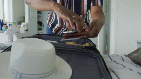 African-american-senior-woman-packing-covid-vaccine-passport-into-suitcase