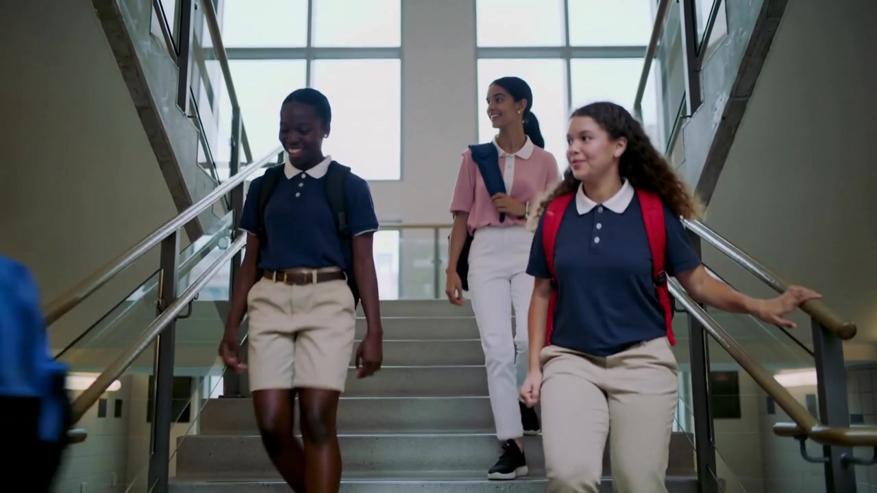Walking students wearing polos starting descent at top landing, touching handrails on school stairs