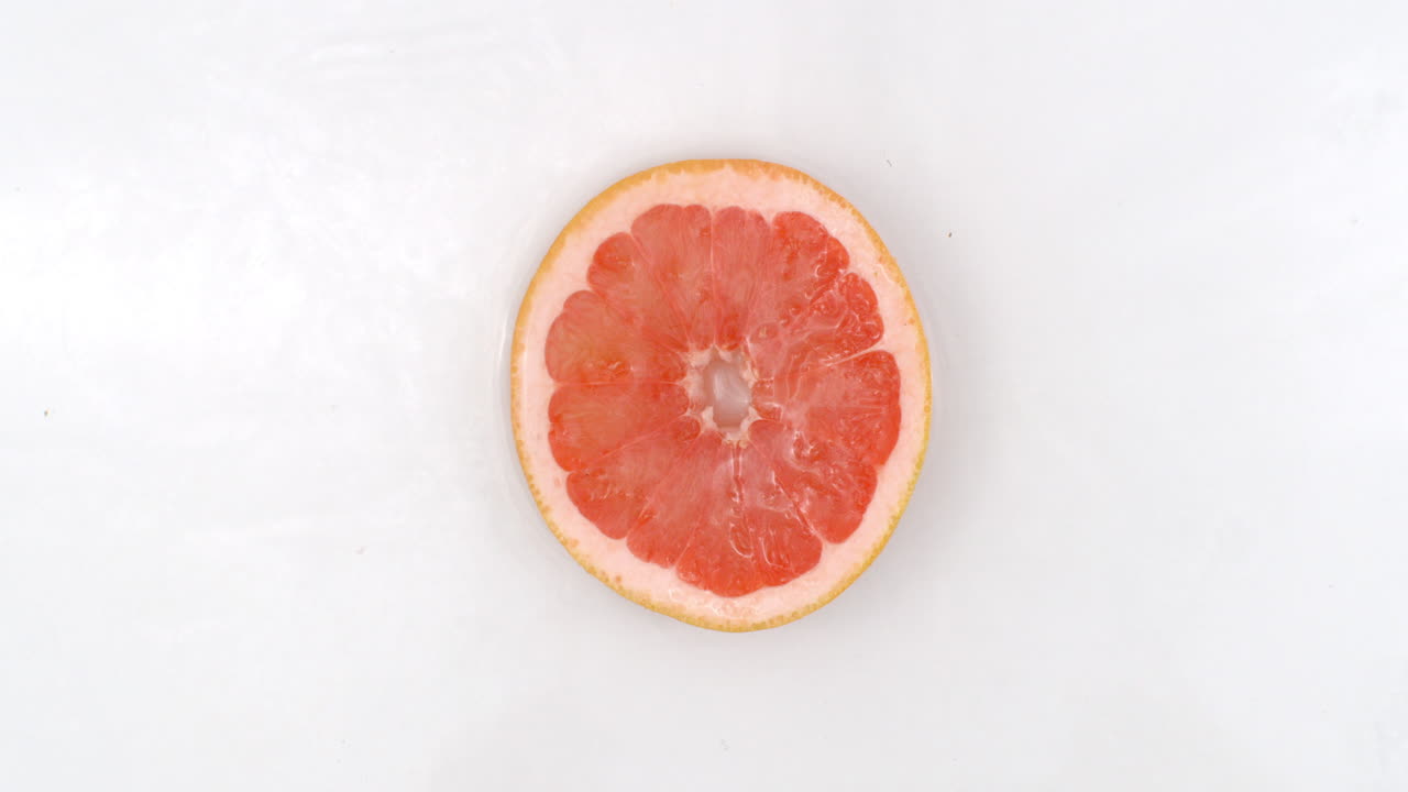 Top view: on a white background a one fresh grapefruit is lying in the water water drops are falling from above and splashes are falling in slow motion in all directions.