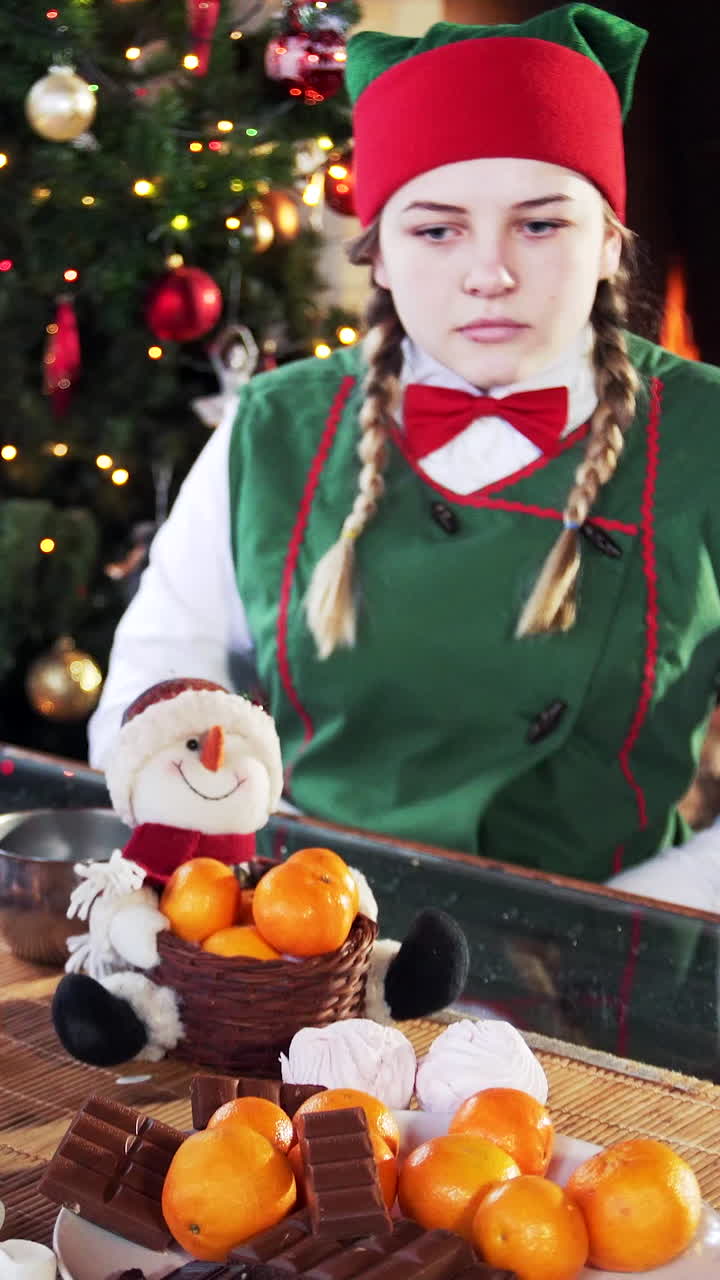 Girl elf tries to take sweets. Funny elves sitting at table on Christmas background. Vertical video