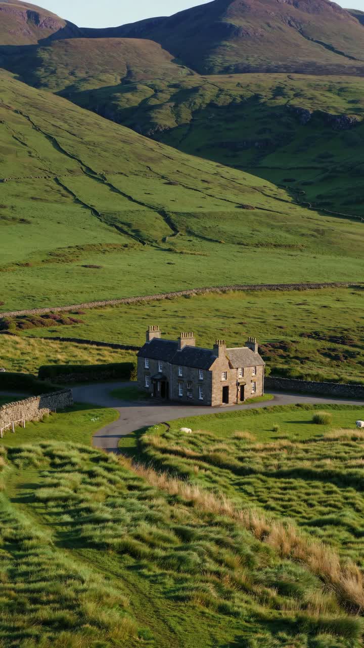 Aerial video still of a solitary stone house amidst lush green hills, showcasing a serene landscape
