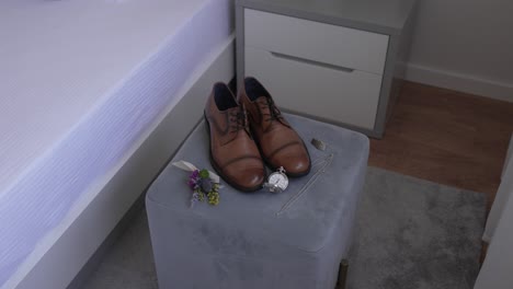 brown dress shoes with watch boutonnière and jewelry on velvet stool