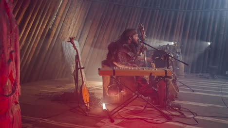 Man-plays-igil-and-sings-old-fold-song-on-stage-with-logs