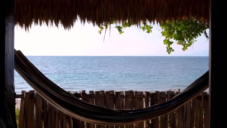 una hamaca balanceándose en la brisa con vistas hermosas al océano desde una tradicional cabaña de alojamiento frente a la playa en un destino de vacaciones de isla tropical remota