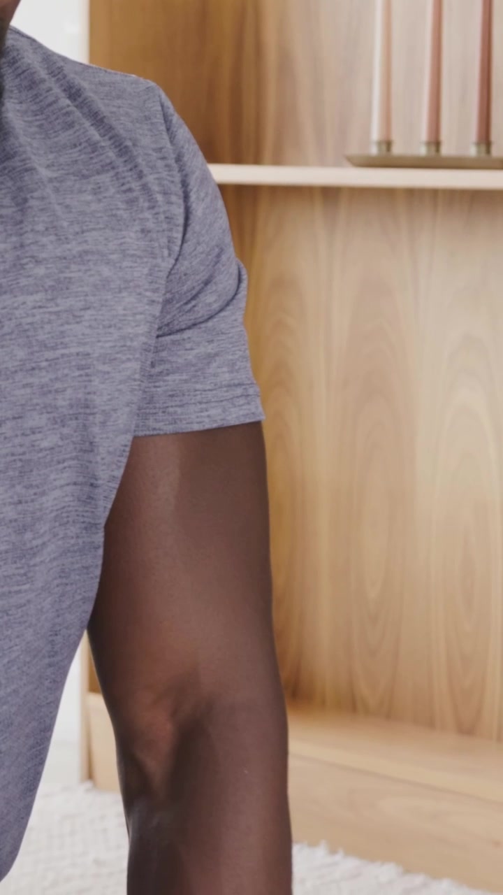 Vertical video: Looking down adult man lowering left arm toward low table at home gray tee candles