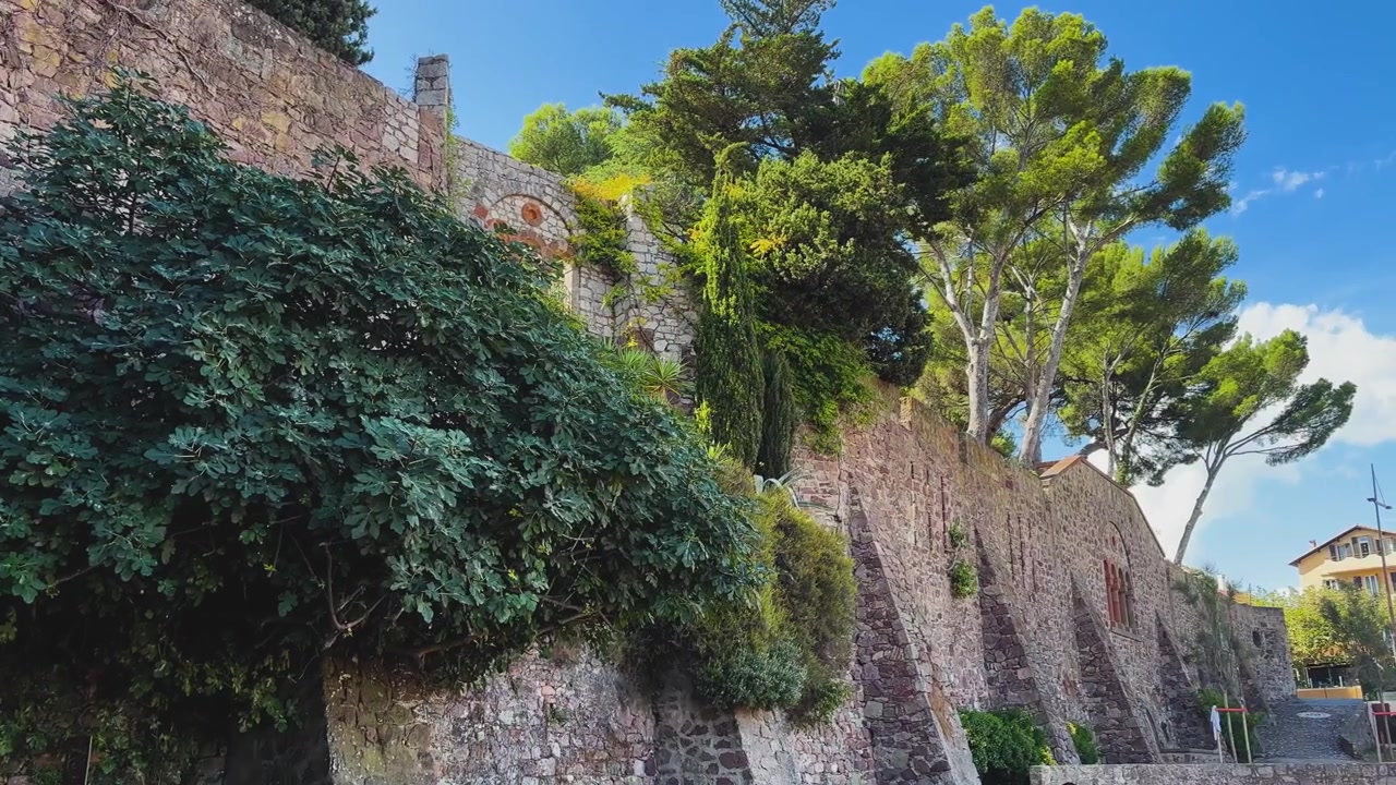 Antichi bastioni in pietra si ergono sotto alti pini mediterranei e una fitta vegetazione in una giornata di sole ad Antibes, Francia.