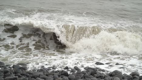 Tilt-down-with-Winter-Tide-splashing-in-over-rocky-beach-at-Dunraven-Bay,-South-Wales