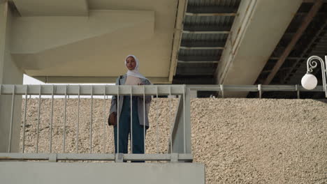 Glückliche-Muslimische-Dame-In-Freizeitkleidung-Winkt-Mit-Der-Hand-Unter-Der-Brücke