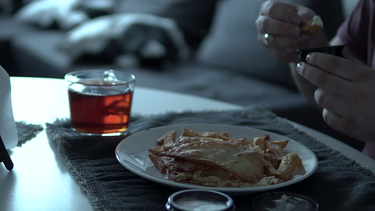 Man eating at home table unhealthy food and drink tea, put chips to sauce