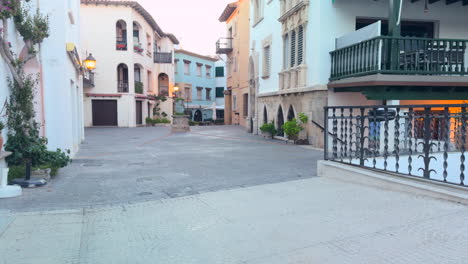 scenic view of a quiet mediterranean plaza surrounded by vibrant facades, wrought iron balconies, arched windows and lush plants in soft evening light. no people, calm atmosphere