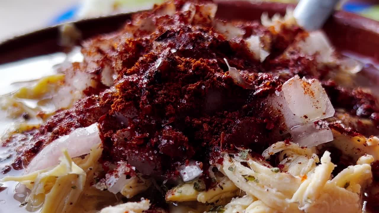 Close-up shot of adding salt and chili to a bowl of pozole