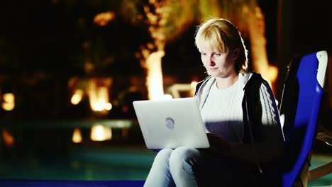una mujer joven usa una computadora portátil junto a la piscina