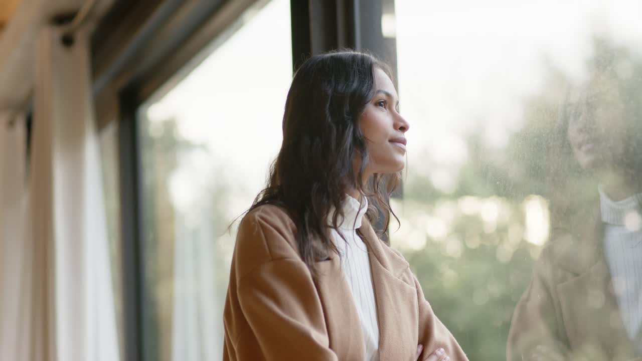 Woman gazing out window in lounge, breathing and smiling at reflection in glass, seeking calm