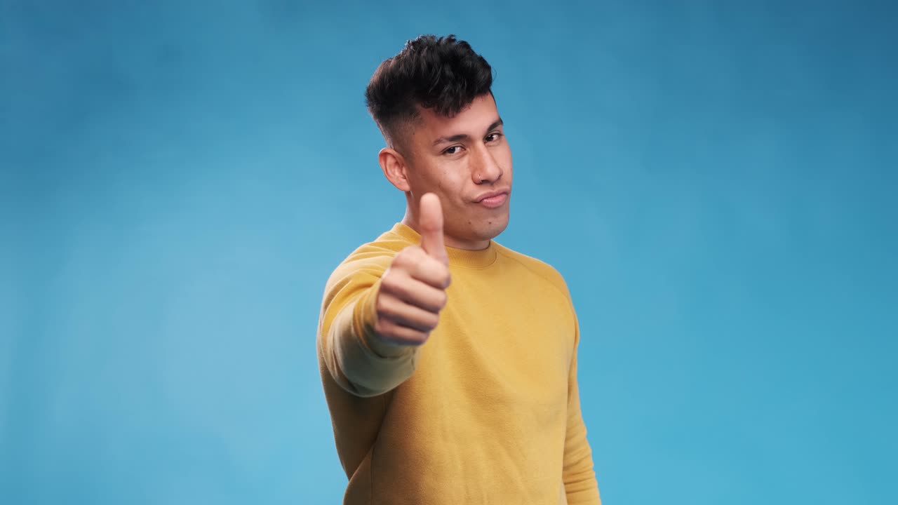Young man with thumb up to show agreement or approval while standing on an isolated background.