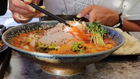 mujer comiendo sopa fría de pescado crudo mulhoe dentro de un restaurante coreano
