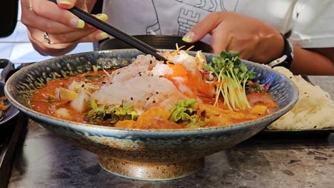 woman eating mulhoe raw fish cold soup inside korean restaurant