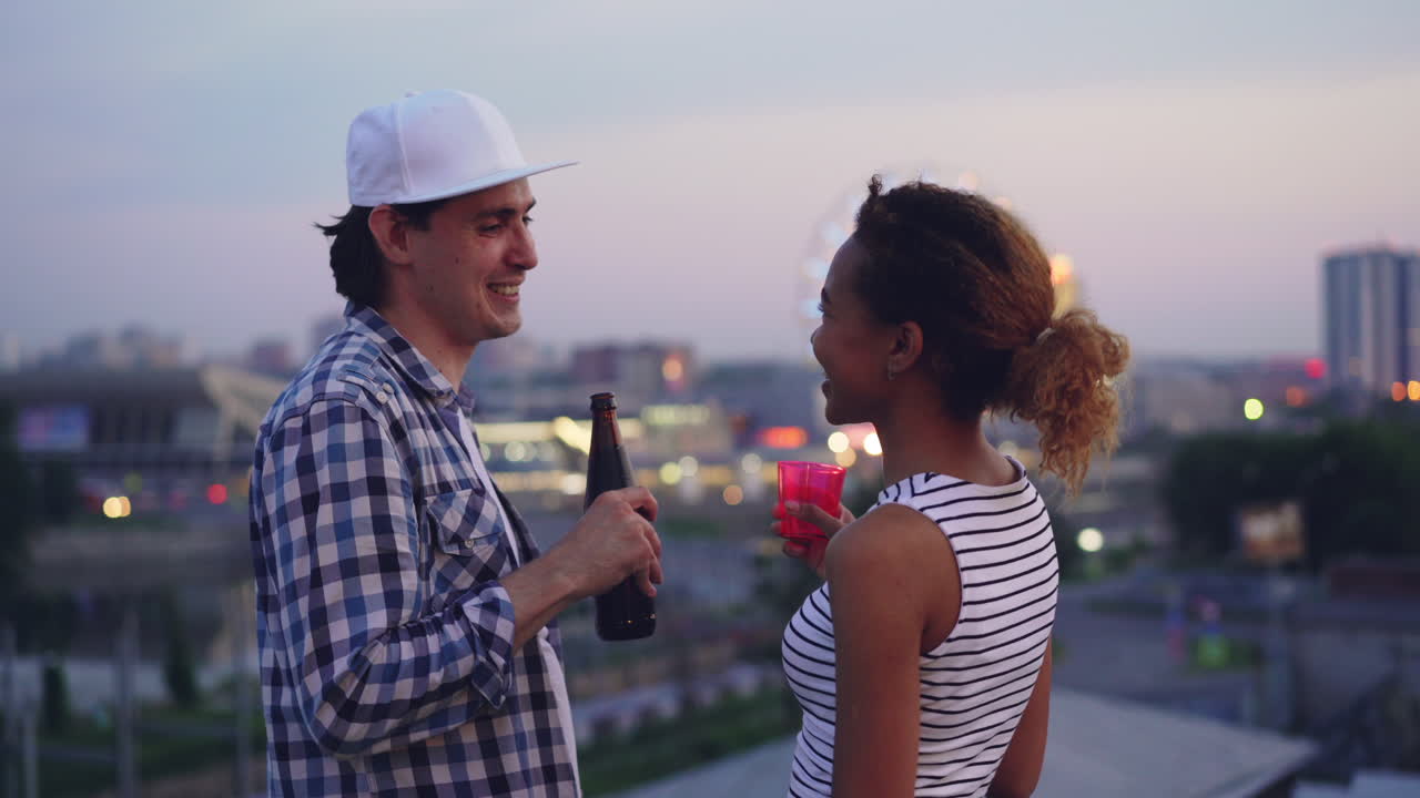Par nyder drinks på tagterrasse ved solnedgang