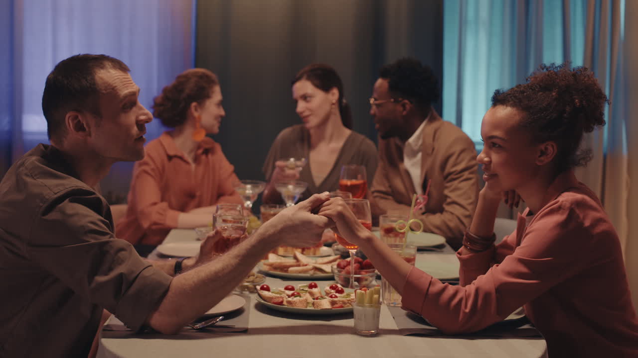 Multiethnic Couple Holding Hands at Friends Dinner Table