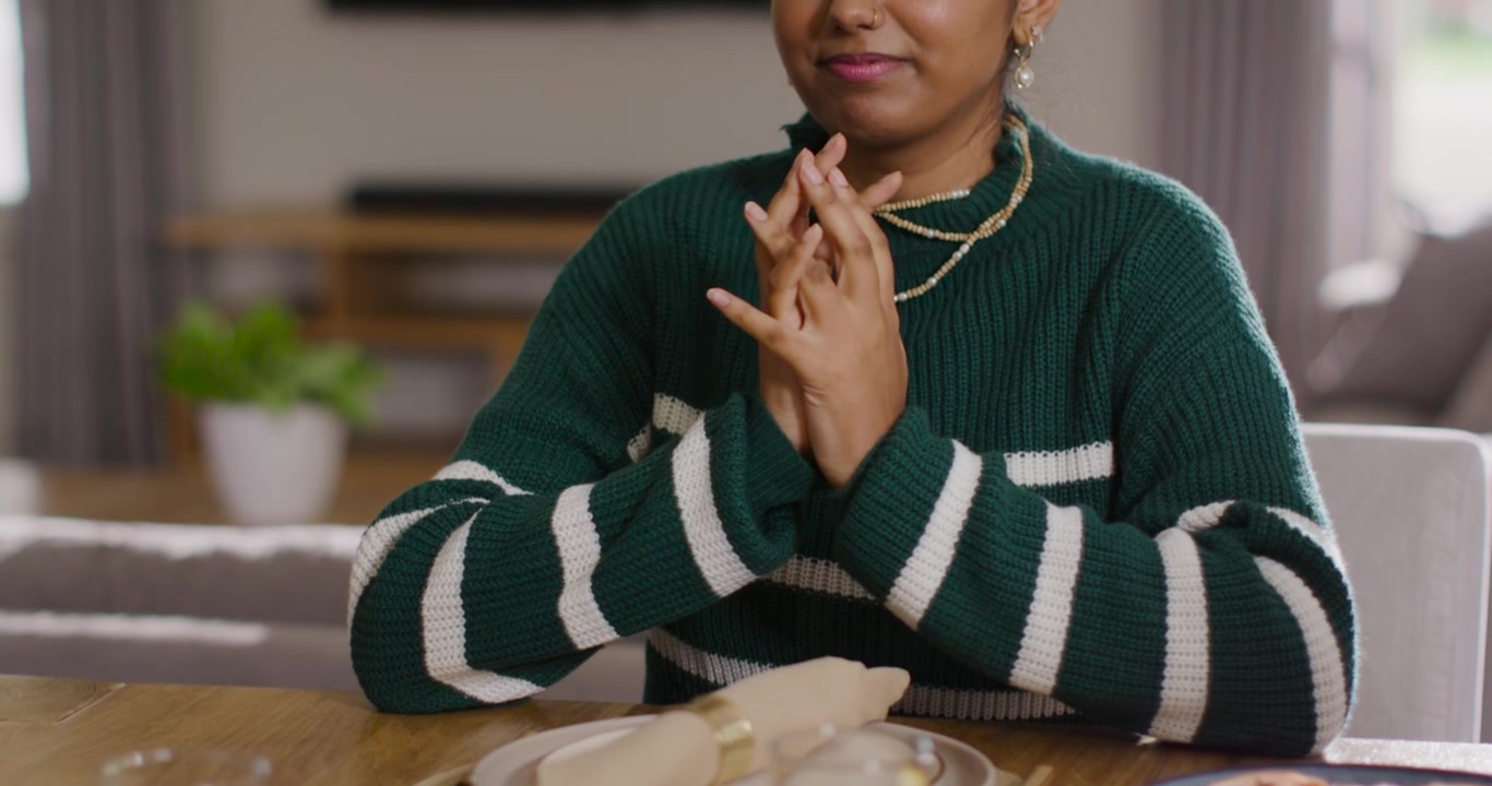 Hands releasing Indian woman in green sweater opening hands, clapping folding at table before meal