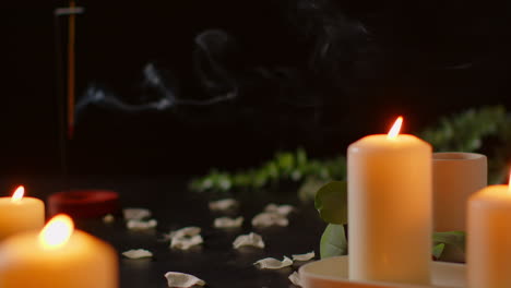 still life of lit candles with scattered flower petals and incense stick against dark background as part of relaxing spa day decor