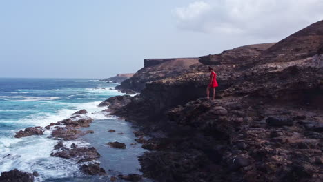 woman a in red dress admires the blue ocean view from a cliff in ajuy