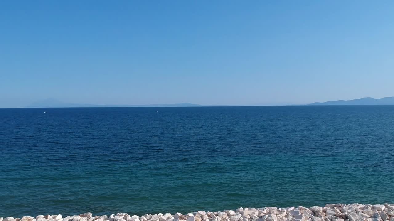 Revealing drone shot over a wave breaker with stones overlooking the ocean on a clear summer day