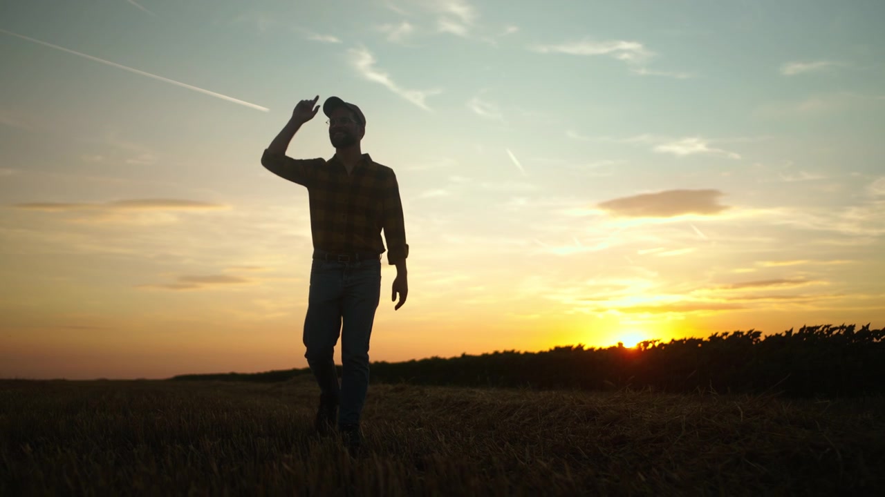 Agricoltore che cammina nel campo raccolto al tramonto