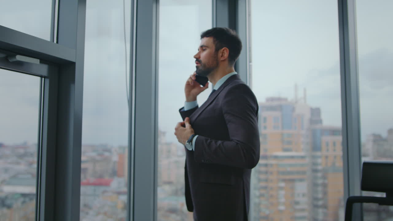 Manager aziendale che parla al cellulare, guardando fuori dalla finestra dell'ufficio. Uomo al telefono.