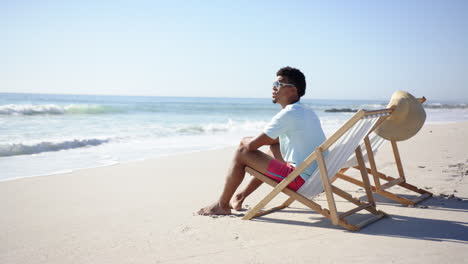 young biracial man relaxes on a beach chair by the sea, with copy space