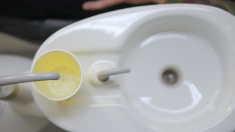 Dental-Spittoon-Sink-Close-Up-Of-Yellow-Plastic-Cup-Being-Filled-With-Water-For-Patient-To-Rinse-Teeth