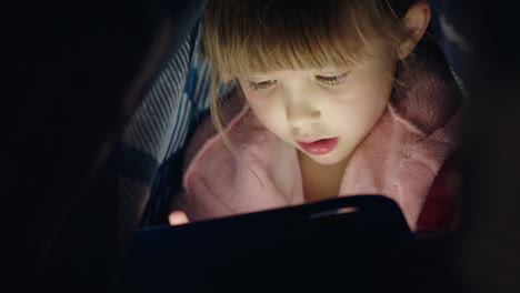 Süßes-Kleines-Mädchen,-Das-Unter-Einer-Decke-Einen-Digitalen-Tablet-Computer-Benutzt-Und-Spaß-Am-Lernen-Auf-Touchscreen-Technologie-Hat,-Indem-Es-Spiele-Spielt-Und-Vor-Dem-Schlafengehen-Spaß-Hat