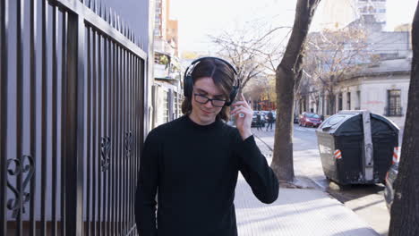 young man with glasses and headphones smiles, walking and listening to music on the street