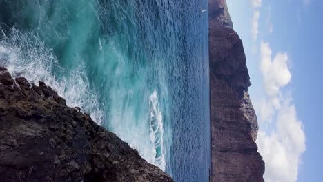 vertical-aerial-of-coastline-with-blue-pristine-clear-ocean-water-crashing-on-the-the-coastline