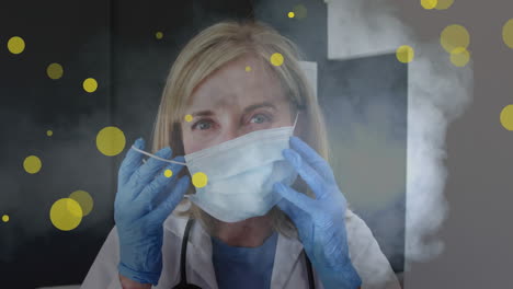 animation of yellow dots over caucasian female doctor in face mask