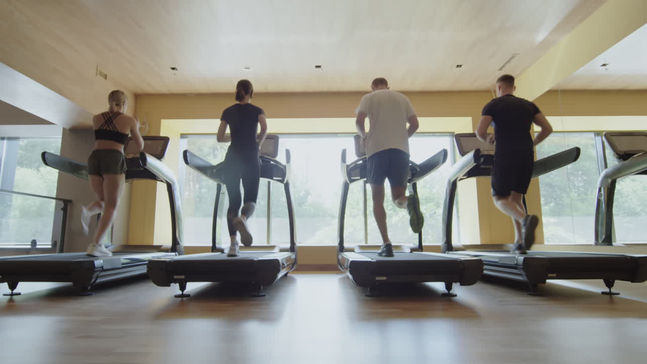 Four people running on treadmills in a modern gym