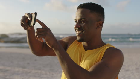 Junger,-Fitter-Afroamerikanischer-Mann,-Der-Mit-Dem-Smartphone-Am-Strand-Fotografiert-Und-Eine-Gelbe-Weste-Trägt