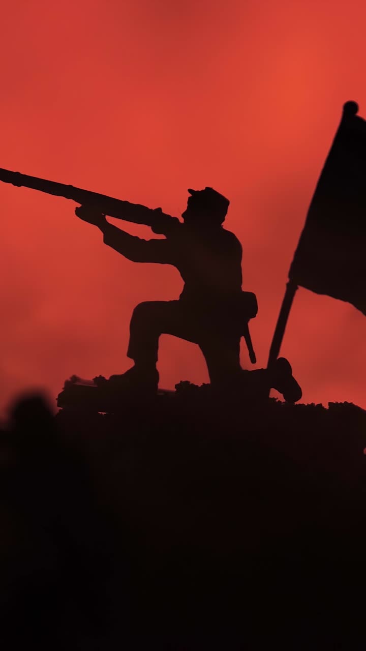 Silhouette of kneeling toy soldier aiming rifle next to large flag in smoky battlefield setting