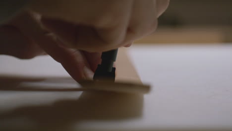 a craftsman presses a pronged leather chisel into a strip of leather, creating evenly spaced holes for stitching in a detailed close-up view.