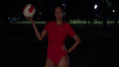 a young girl in a bikini is holding a football in her hand during the night
