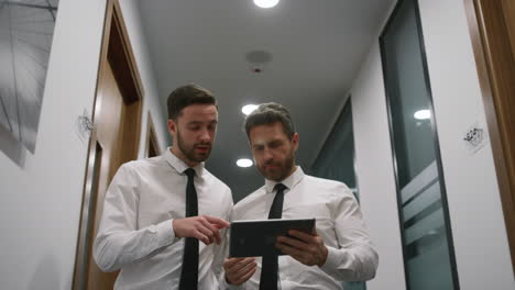 Couple-managers-discussing-business-project-using-tablet-pad-in-office-hallway.