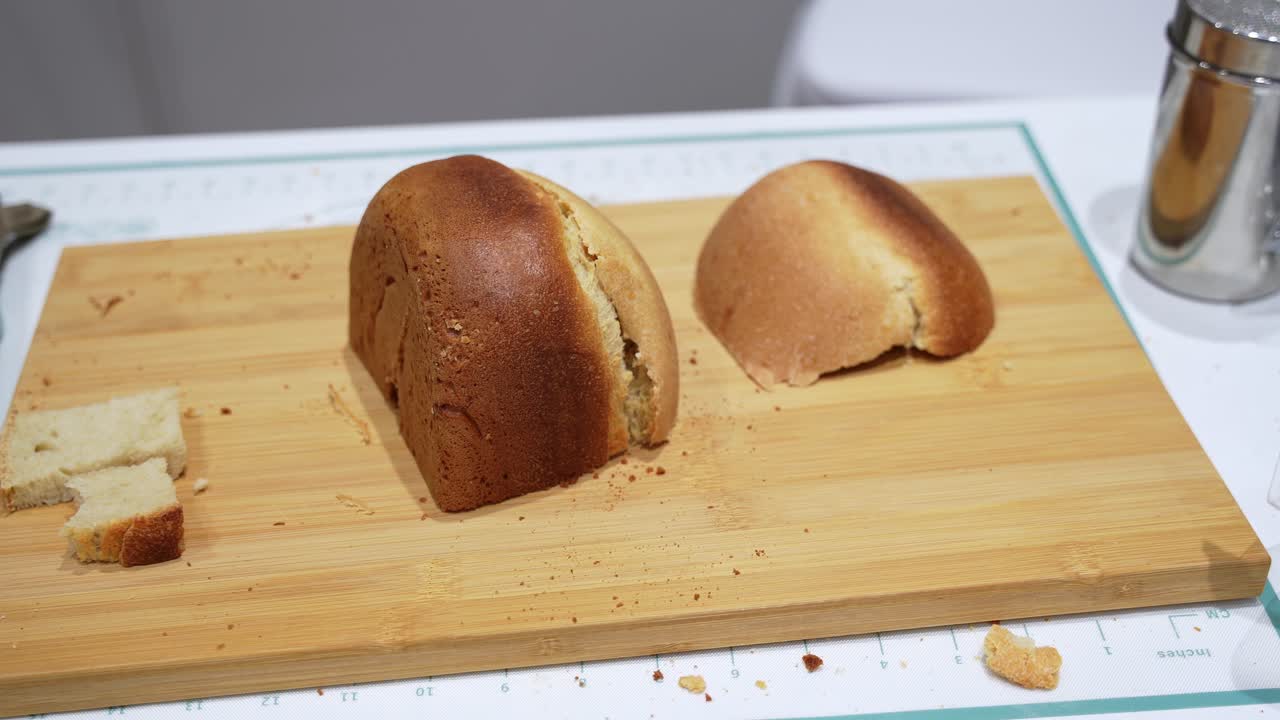 Close up of a freshly baked homemade bread loaf with golden brown crust resting on a wooden cutting board, showing crumbs and soft interior texture in a kitchen environment
