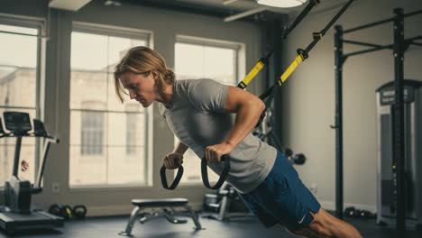 a focused workout session featuring a young man utilizing trx suspension training for strength and muscle building in a modern gym environment