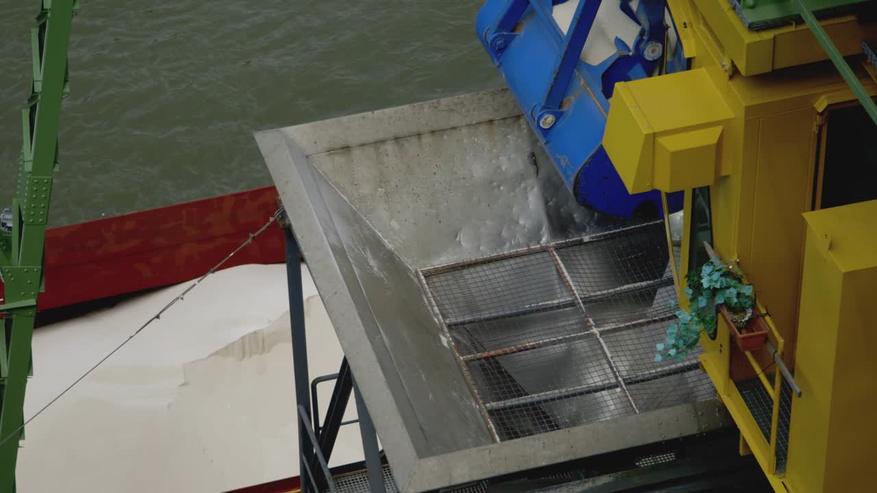 Una gru scarica una nave piena di fertilizzante in un porto e lo fa cadere in un imbuto