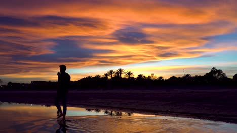 man walking on the water towards the bottom of the beach, the cloudy sky with beautiful colors at sunset on the background of the image