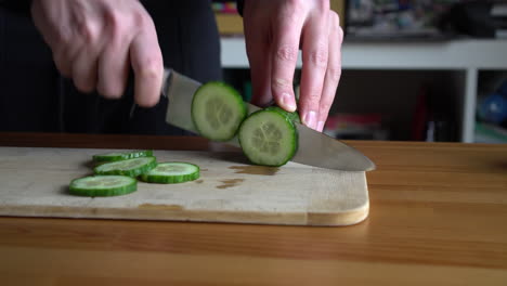 Man-chef-cutting-cucumber-on-chopping-wooden-board