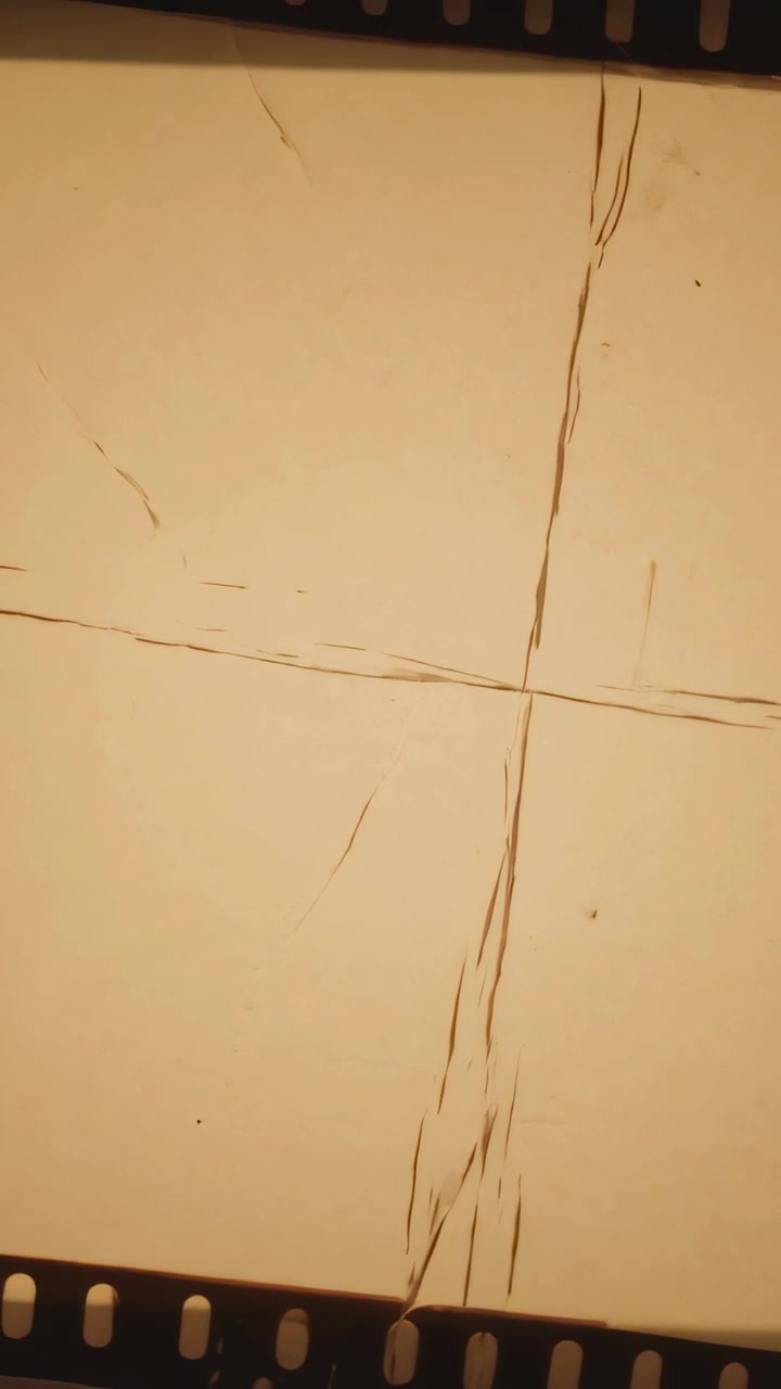 Video verticale: Telecamera che si sposta e spinge una pellicola da 35mm su un tavolo luminoso, mostrando graffi a X e polvere per la revisione.