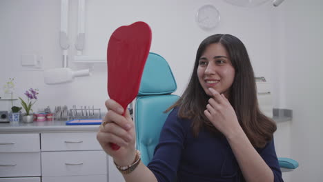 Happy-Patient-looking-up-her-teeth,-she-checks-her-smile-in-the-mirror-and-certify-the-good-job-done-by-the-dentist