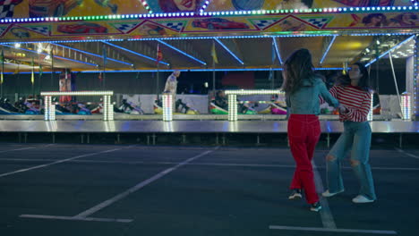 cheerful girls dancing funfair at illuminated carousel. happy best friends fun