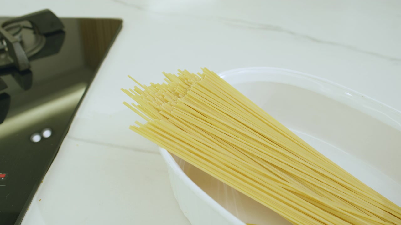 Primo piano che mostra una mano che seleziona spaghetti gialli secchi da un contenitore.