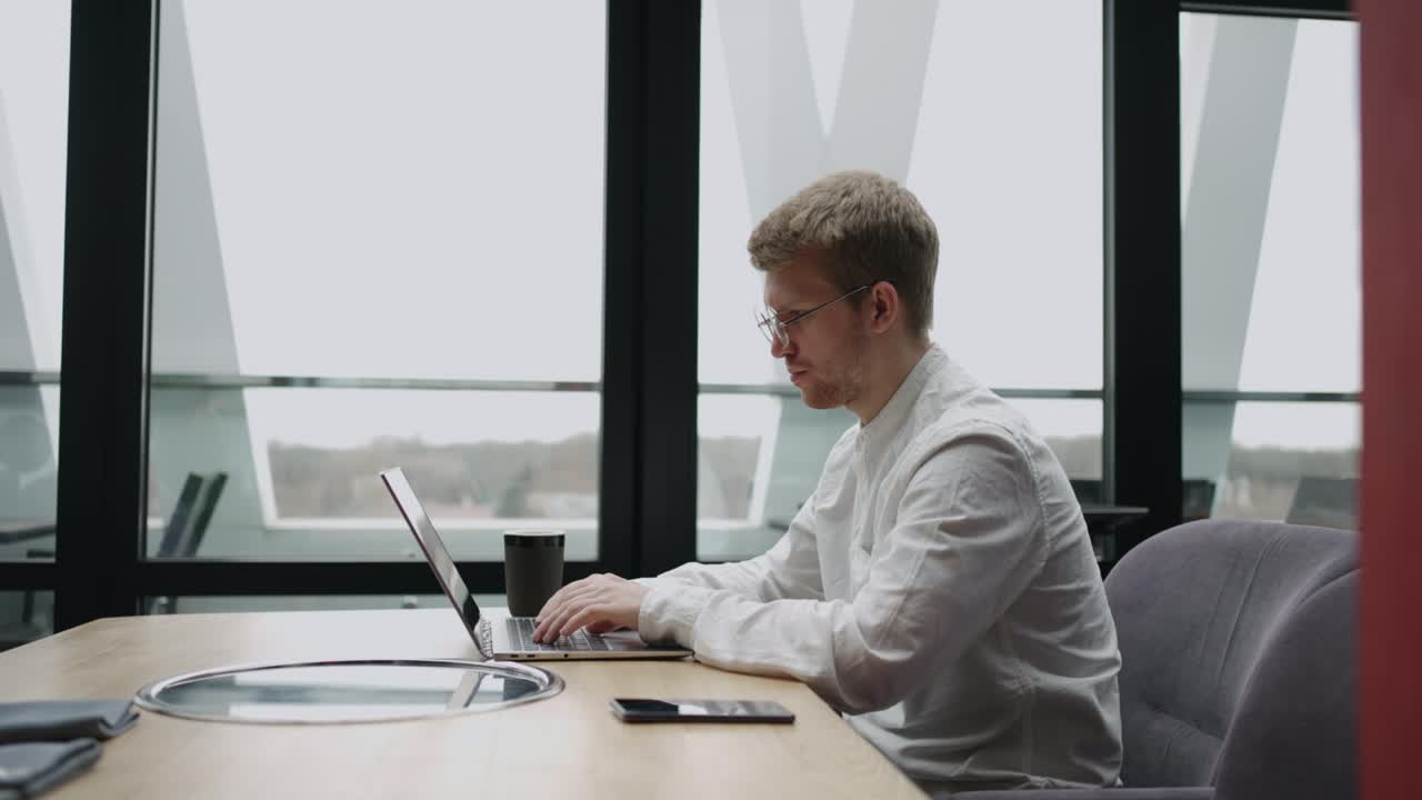 un hombre adulto está trabajando solo en una oficina moderna, usando una computadora portátil con conexión inalámbrica a internet para buscar información
